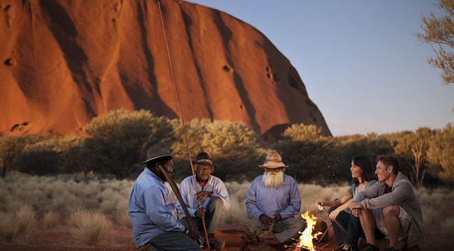 People sitting fireside before Uluru