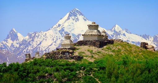 Beautiful scenic view - green hill with old white buddhist stupa against the background of colorful mountain range covered with snow and blue sky